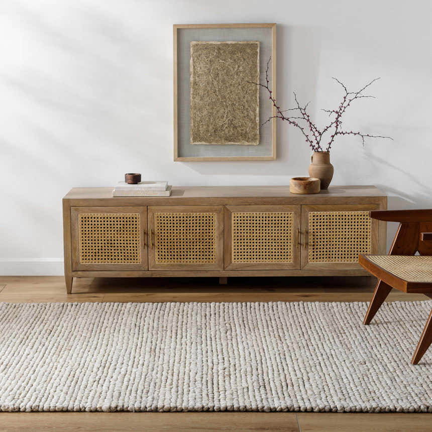 Living room scene with a beige Olisa Cream Wool Area Rug, wood cabinet, and modern chair. Roomscene-Rectangle