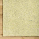 Close-up of Isako Solid Lime Washable Area Rug showing texture and color variations on light wood floor. Corner