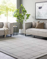 Living room scene with light gray sofas and a Siarl Gray Checkered Area Rug. Modern decor with a tree and neutral tones. Roomscene-Rectangle