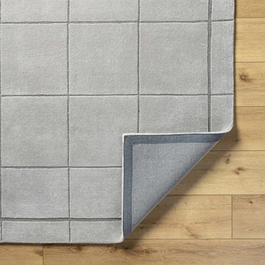 Close-up of the Siarl Gray Checkered Area Rug. The hand-tufted wool rug has a light gray grid pattern on a wood floor. Fold