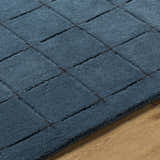 Close-up of the Sanvi Navy Wool Area Rug showing its hand-tufted texture and contemporary black grid pattern on a wood floor. Texture
