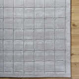 Close-up of the Sanvi Gray Area Rug showing a charcoal grid pattern and soft wool texture on a wood floor. Swatch