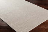 Close-up of the Edith Premium Rug in beige on dark wood floors. Hand-woven, contemporary style. Corner