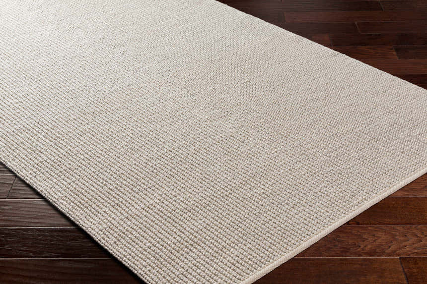 Close-up of the Edith Premium Rug in beige on dark wood floors. Hand-woven, contemporary style. Corner
