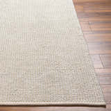 Close-up of the hand woven Edith Premium Rug in beige on a wood floor, showcasing texture and contemporary style. Front