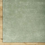 Close-up of the sage Helio Area Rug showing its subtle horizontal texture and soft viscose material on a wood floor. Corner