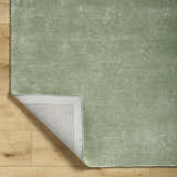 Close up of the sage Helio Area Rug showing texture and backing on light wood floor. Fold