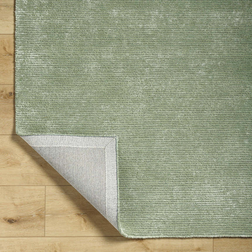Close up of the sage Helio Area Rug showing texture and backing on light wood floor. Fold