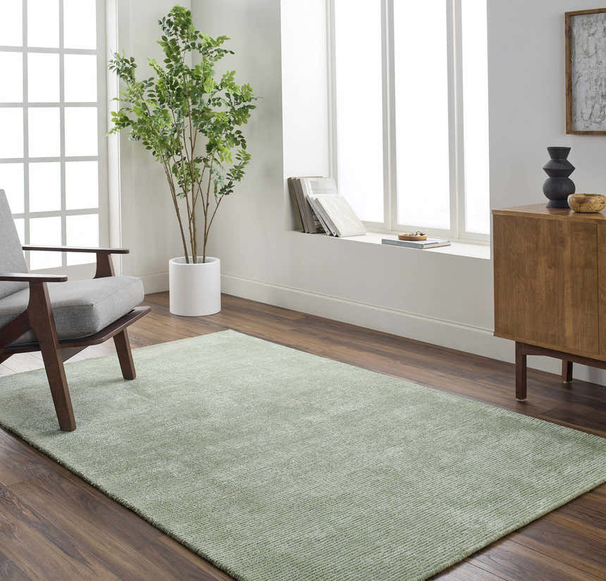 Sage Helio Area Rug in a bright living room with grey chair, wood cabinet, and large window. Roomscene-Rectangle