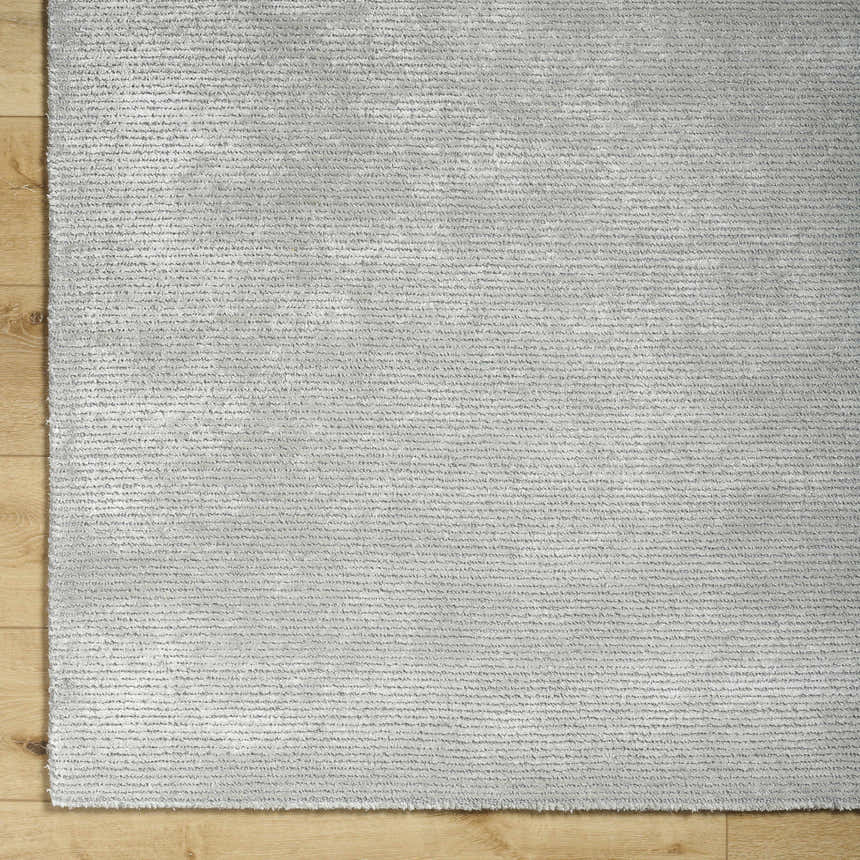 Close up of the hand tufted Noham Area Rug in metallic silver and pale slate on hardwood floor. Corner