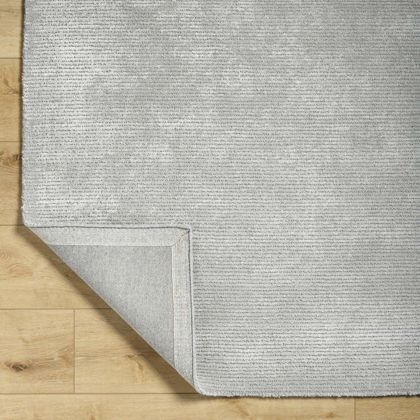 Close-up of the hand-tufted Noham Area Rug in metallic silver, pale slate, and silver gray on a wood floor. Fold
