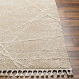 Close-up of the Hosea Cream Area Rug showing the geometric pattern, soft texture, and tassel fringe on wood flooring. Front