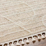Close-up of the beige Inaya Area Rug showing its geometric pattern, shaggy texture, and decorative tassels. Texture