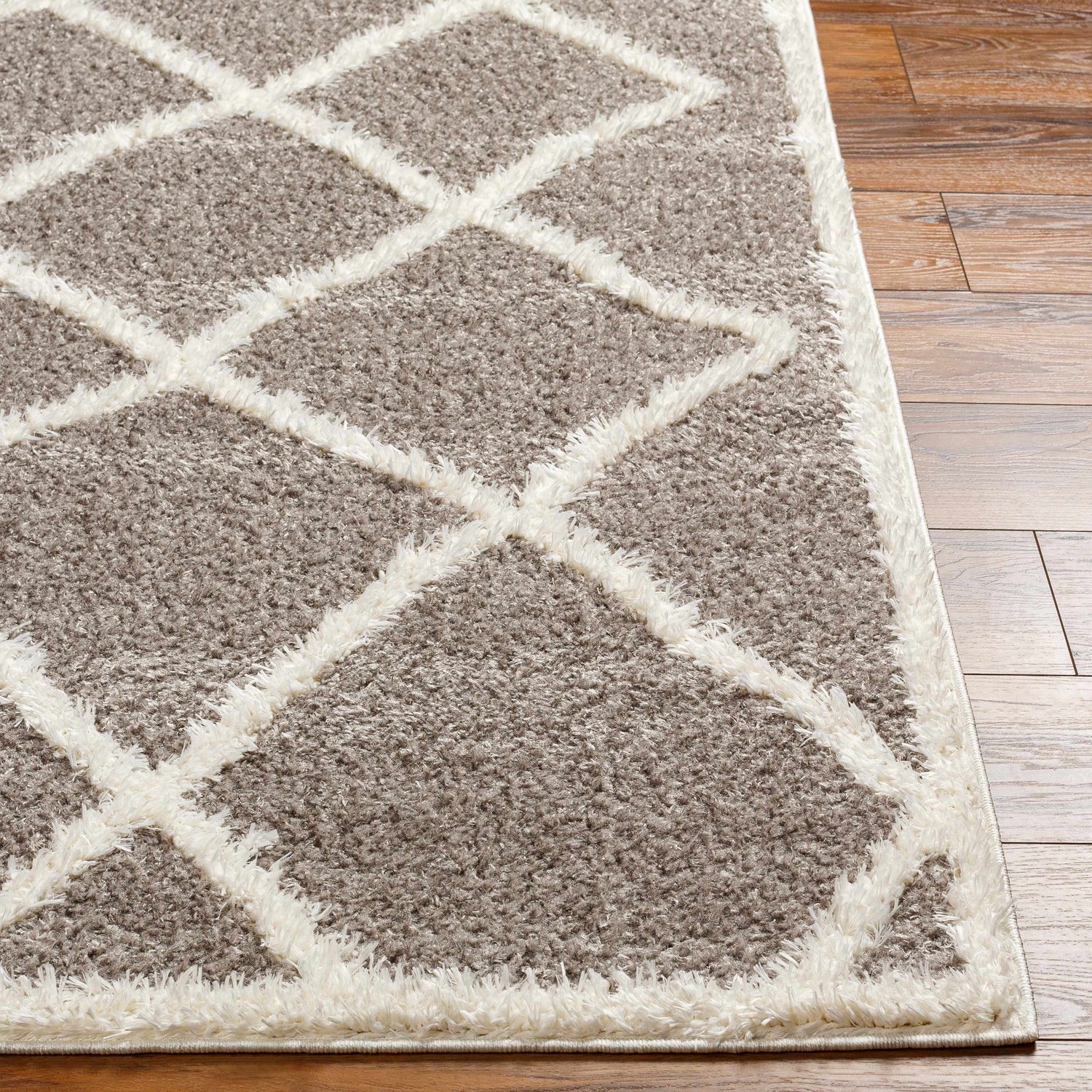 Close-up of the Alkas Area Rug showing its dark gray shag texture and off-white geometric diamond pattern. Front
