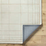Close-up of the Sedna Wool Area Rug showing its medium gray and tan grid pattern and hand-tufted texture. Fold