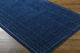 Close-up of the Sedna Navy Wool Area Rug. Hand-tufted wool rug with a geometric, grid-like pattern in navy and gray. Corner