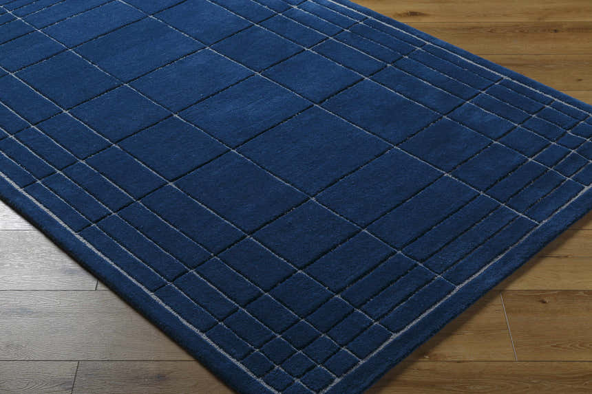 Close-up of the Sedna Navy Wool Area Rug. Hand-tufted wool rug with a geometric, grid-like pattern in navy and gray. Corner