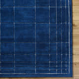 Close-up of the hand-tufted Sedna Navy Wool Area Rug. Features a contemporary grid pattern on a rich navy blue wool texture. Corner