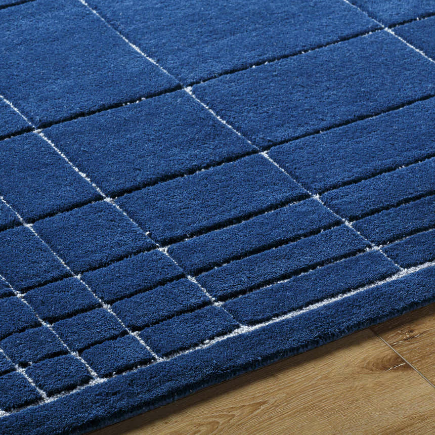 Close-up of the Sedna Navy Wool Area Rug. Features a geometric pattern in navy with gray lines on a wood floor. Texture