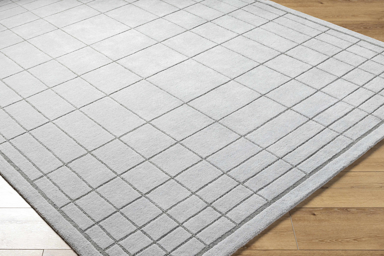 Close-up of Sedna Gray Wool Area Rug. Hand-tufted wool rug with a geometric square pattern in medium gray on wood floor. Corner