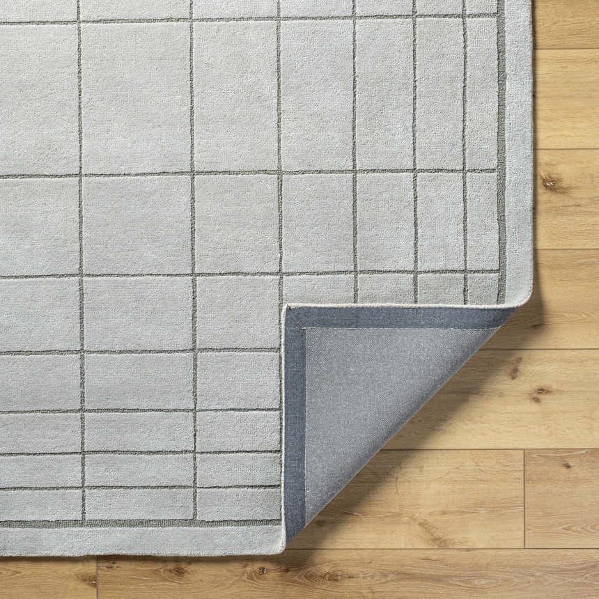 Close-up of the Sedna Gray Wool Area Rug showing its gray grid pattern and hand-tufted texture on a light wood floor. Fold