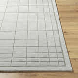 Close-up of the Sedna Gray Wool Area Rug featuring a grid pattern on a light wood floor. Front