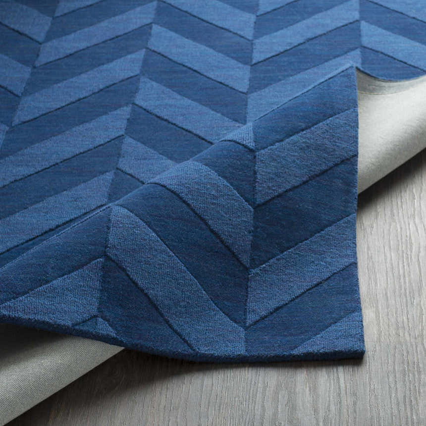 Close-up of the navy Searsmont Area Rug showing its textured chevron pattern and backing on a wood floor. Clearance item. Fold