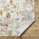 Close up of the Ouida Floral Rug showing a light silver, copper, and gold leaf pattern. Fold