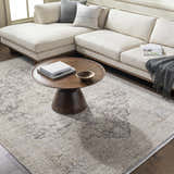 Living room scene with a beige Njeri Area Rug, a round wood coffee table, and a cream-colored sectional sofa. Roomscene-Rectangle