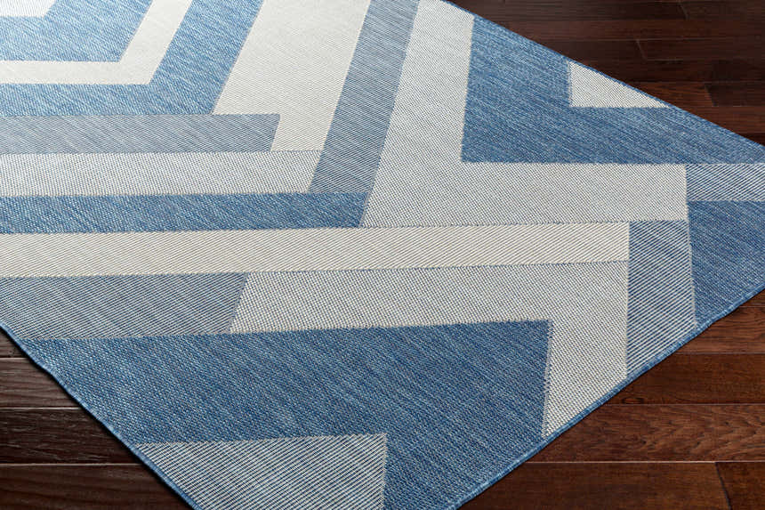 Close up of the Adwen Blue Area Rug showing its contemporary geometric pattern and woven texture on dark wood flooring. Corner