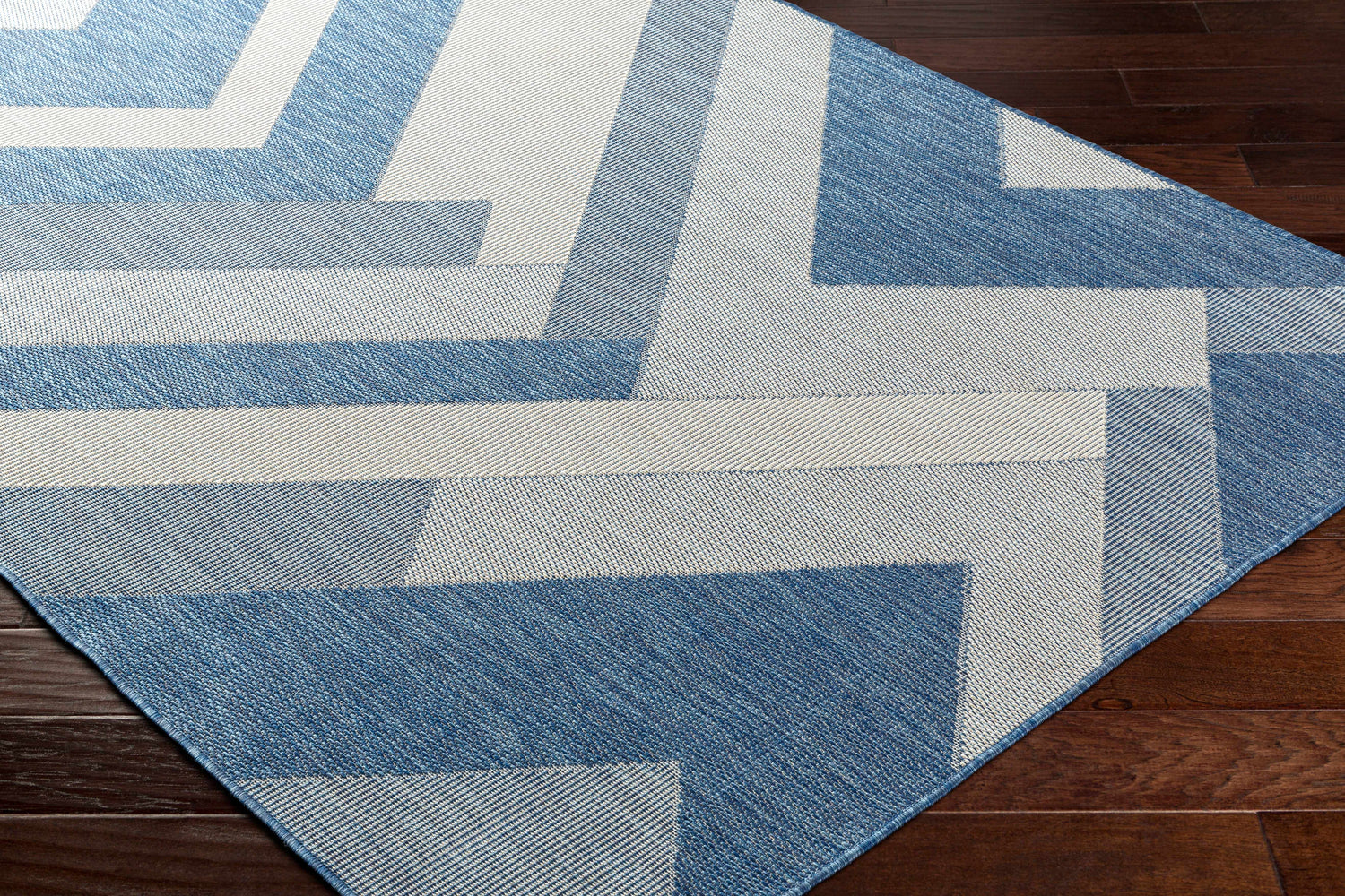 Close up of the Adwen Blue Area Rug showing its contemporary geometric pattern and woven texture on dark wood flooring. Corner
