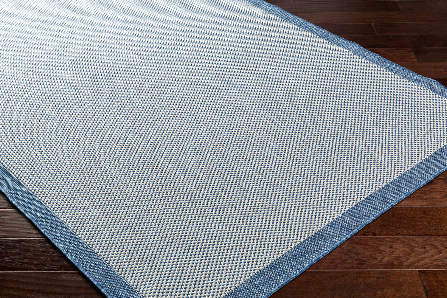 Close-up of the Aleid Blue Area Rug showing its woven texture and denim border on dark wood floors. Corner