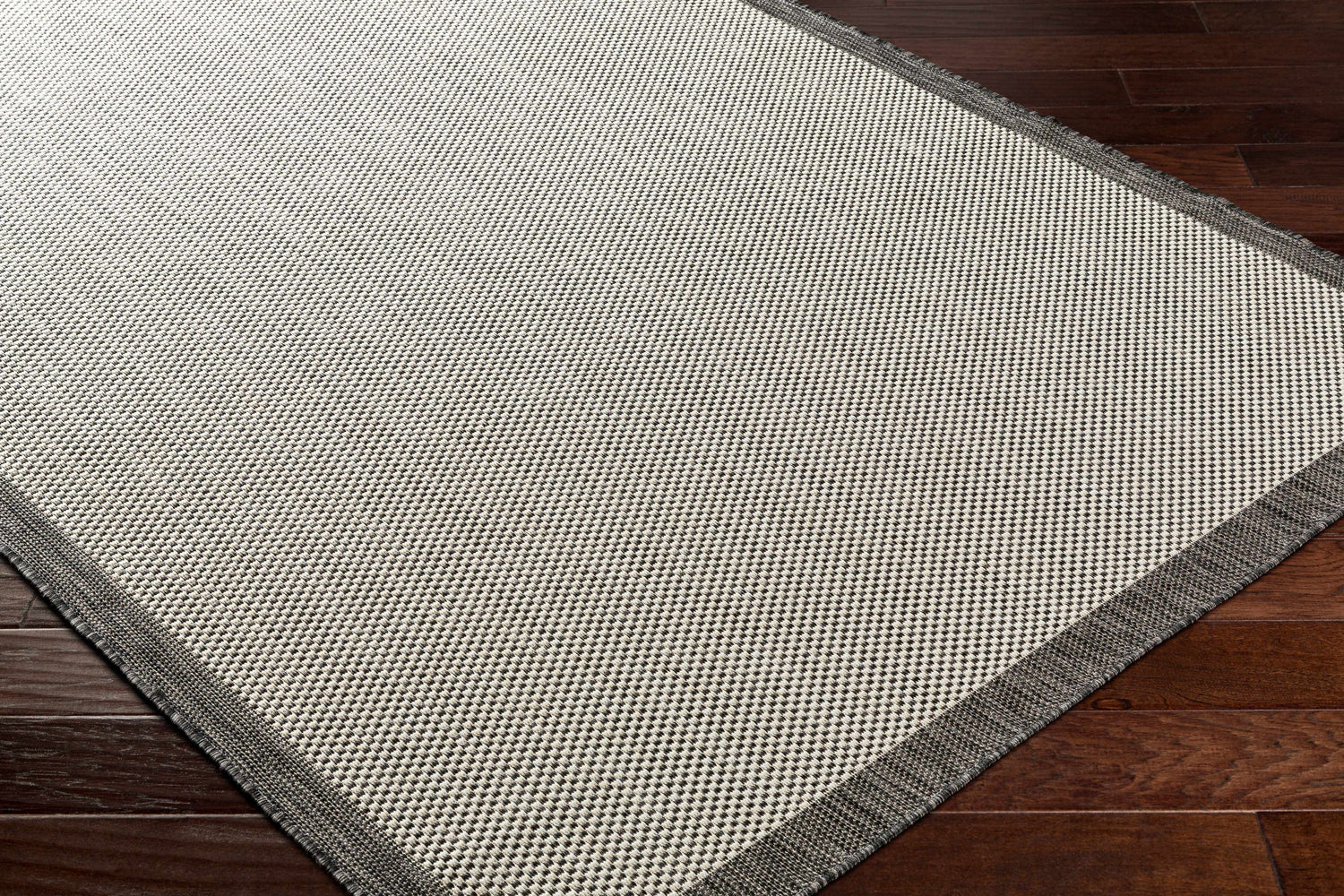 Close-up of the Aleid Gray Area Rug showing its bone and charcoal woven texture and dark gray border on dark wood floor. Corner