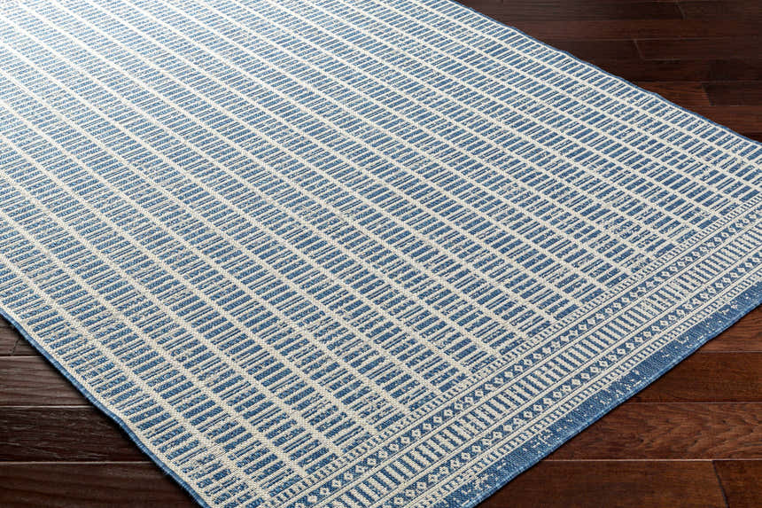 Close-up of the Amena Blue Area Rug showing a geometric block pattern and traditional border on a dark wood floor. Corner