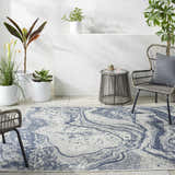 Outdoor patio scene with a Basma Blue Marble Area Rug, gray wicker chairs, a small table, and potted plants. Roomscene-Rectangle