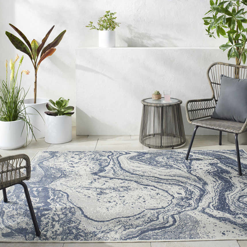 Outdoor patio scene with a Basma Blue Marble Area Rug, gray wicker chairs, a small table, and potted plants. Roomscene-Rectangle