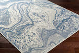 Close-up of the Basma Blue Marble Area Rug showing its abstract marble pattern and blue and gray colors on a dark wood floor. Corner