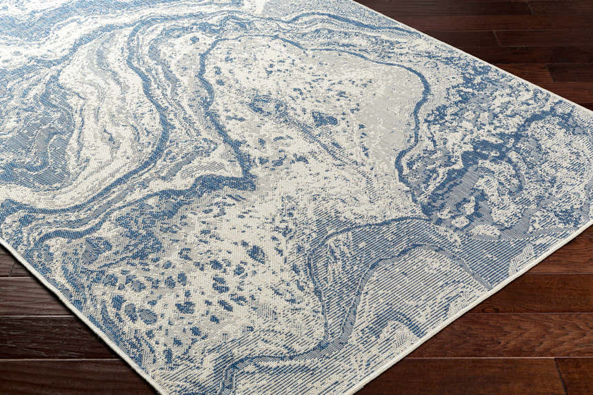Close-up of the Basma Blue Marble Area Rug showing its abstract marble pattern and blue and gray colors on a dark wood floor. Corner