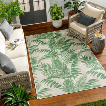 Coastal patio scene with Caley Area Rug, wicker furniture, wood floors, and lush green plants. Roomscene-Rectangle