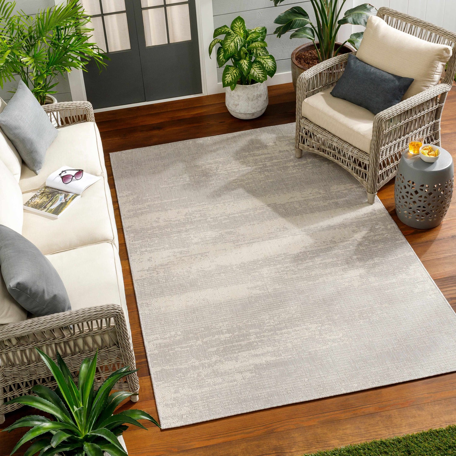 Relaxing patio scene with Cline Cream Area Rug, wicker furniture, wood floors, and potted plants. Roomscene-Rectangle