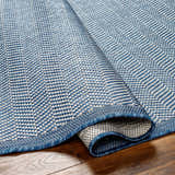 Close-up of the Genet Blue Area Rug showing its woven texture and geometric pattern in denim and white hues. Fold