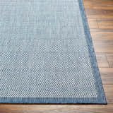 Close-up of the Genet Blue Area Rug showing its denim blue and white herringbone pattern and textured weave. Front