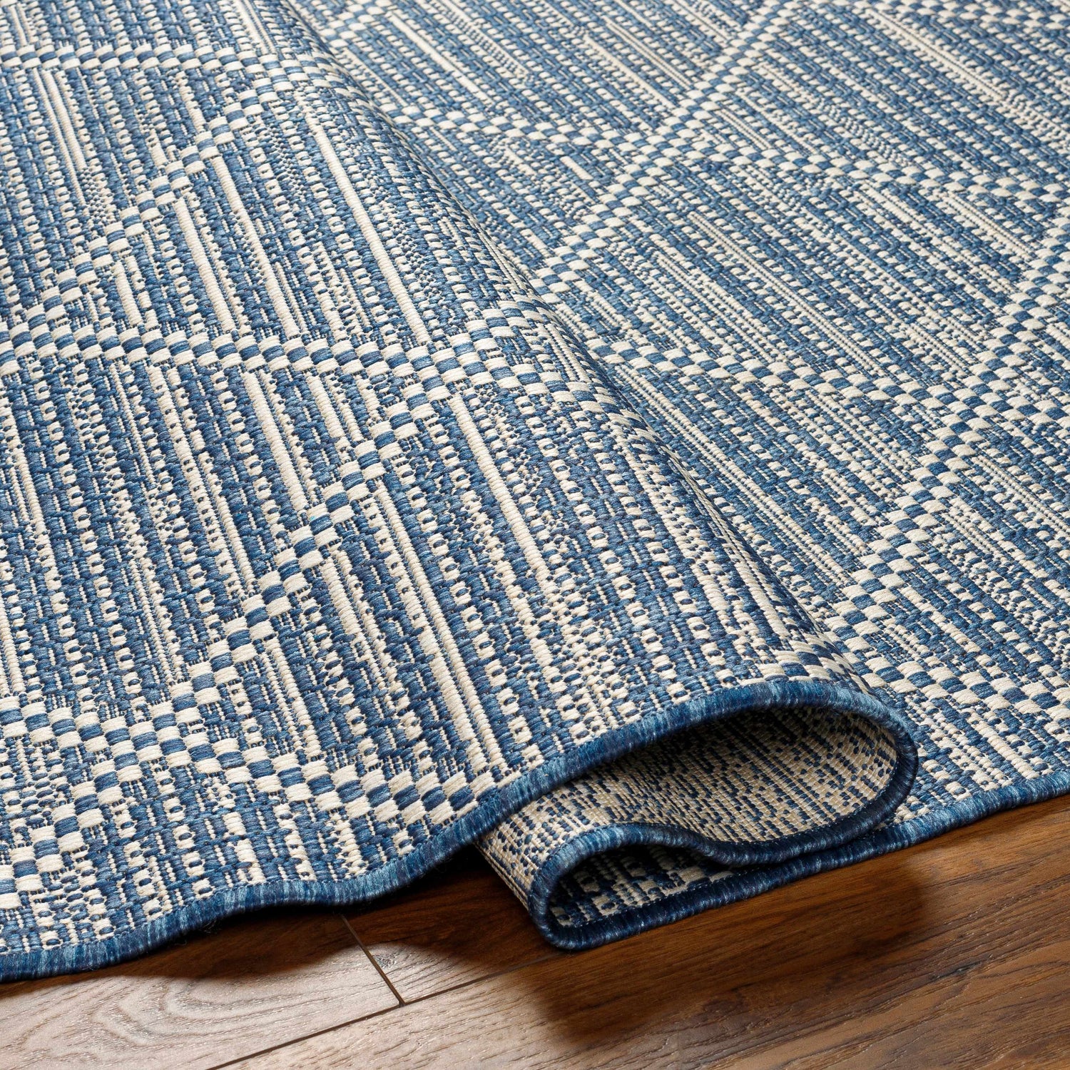 Close-up of the Ivora Blue Area Rug showing its woven texture, denim and natural gray colors, and geometric pattern. Fold