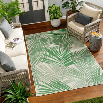 Coastal porch scene with Jaala Area Rug. Beige sofa, wicker chair, and green palm leaf rug. Roomscene-Rectangle