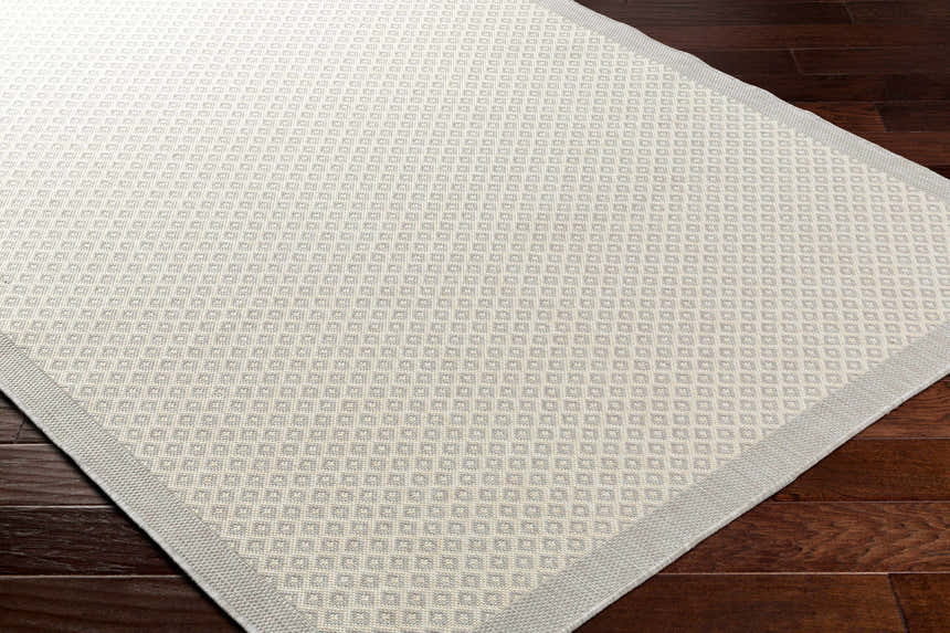 Close-up of the Suzu Area Rug showing a contemporary beige and gray diamond pattern on dark wood floors. Corner