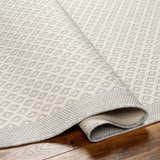 Close-up of the Suzu Area Rug showing its woven diamond pattern and neutral beige, gray, and bone colors. Fold