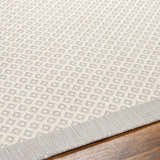 Close-up of the Suzu Area Rug showing a geometric diamond pattern in beige, bone, and gray on a wood floor. Texture