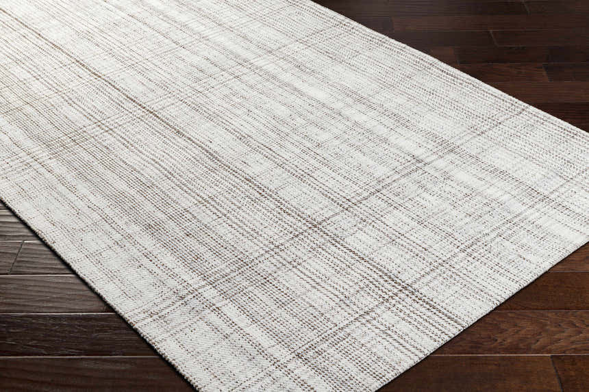 Close up of Jezel Beige Area Rug showing woven texture and subtle plaid pattern on dark wood floor. Corner