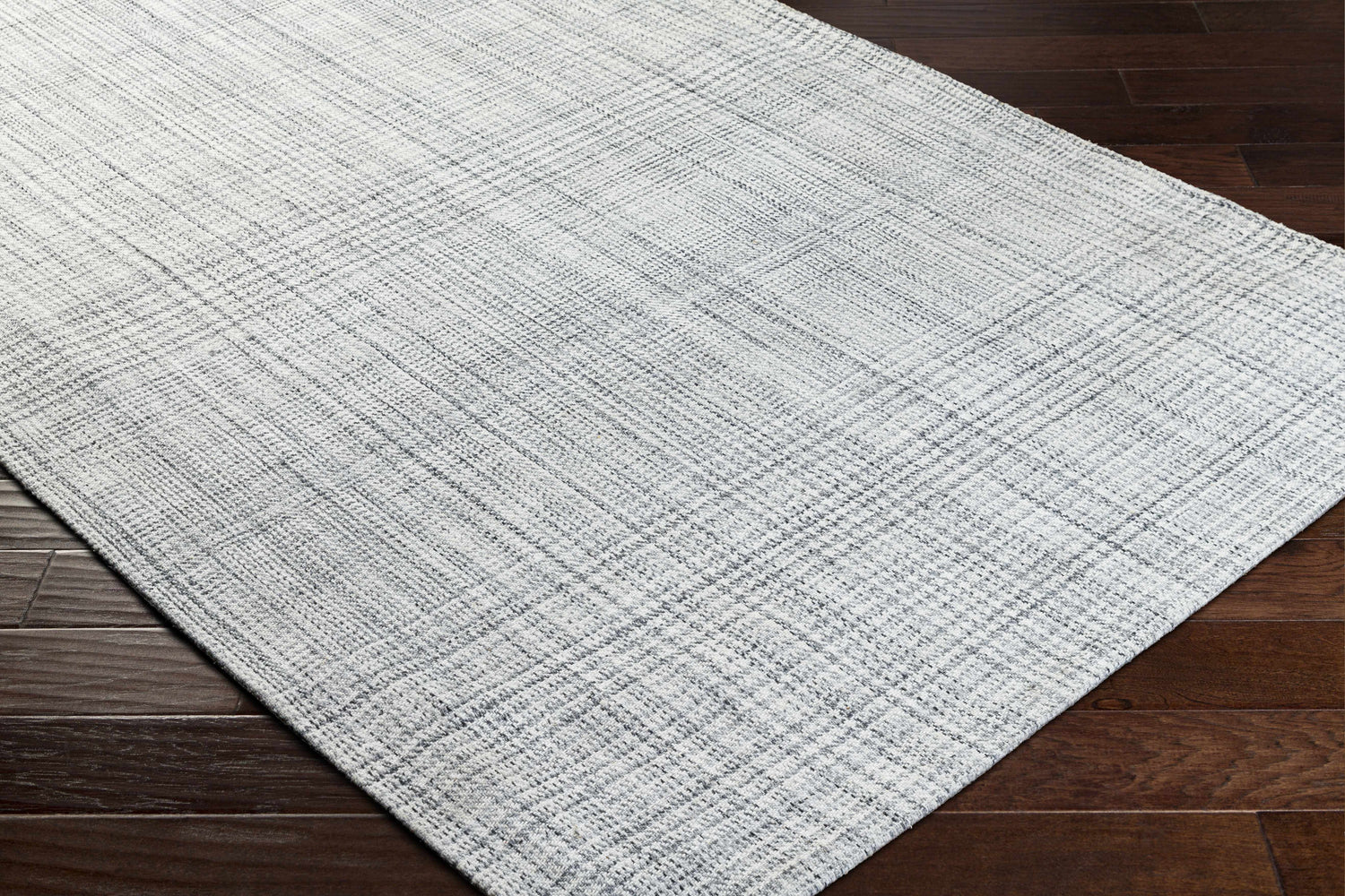 Close up of the Jezel Gray Area Rug showing a woven, textured pattern in gray and white on dark wood floors. Corner