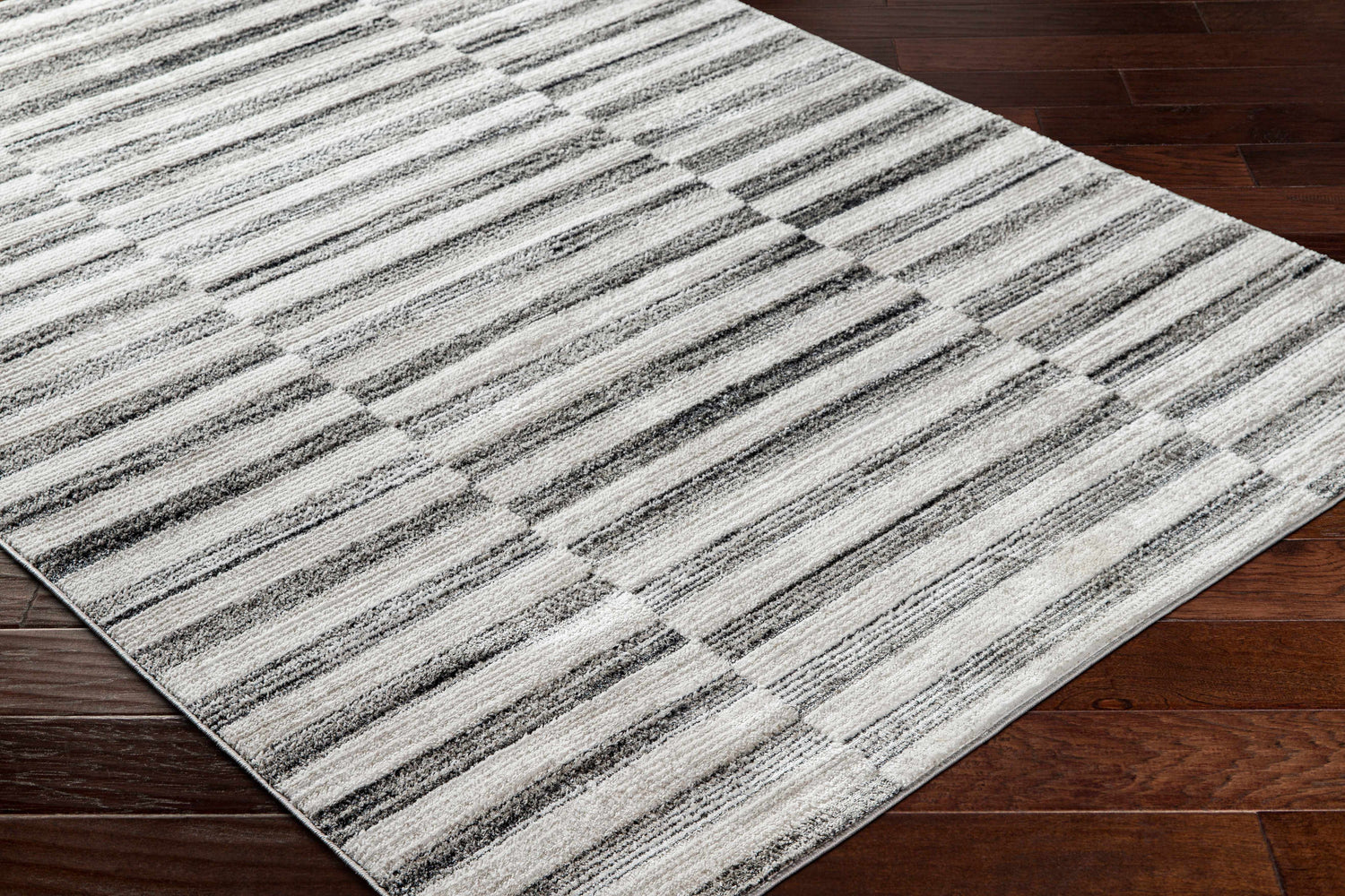 Close-up of the Gorou Taupe Area Rug showing its striped geometric pattern and soft texture on dark wood flooring. Corner
